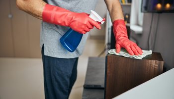 Man tending to household by cleaning his flat Cropped photo of man wearing rubber gloves and spraying cleaning liquid on the surfaces and wiping them