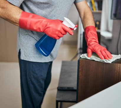 Cropped photo of man wearing rubber gloves and spraying cleaning liquid on the surfaces and wiping them
